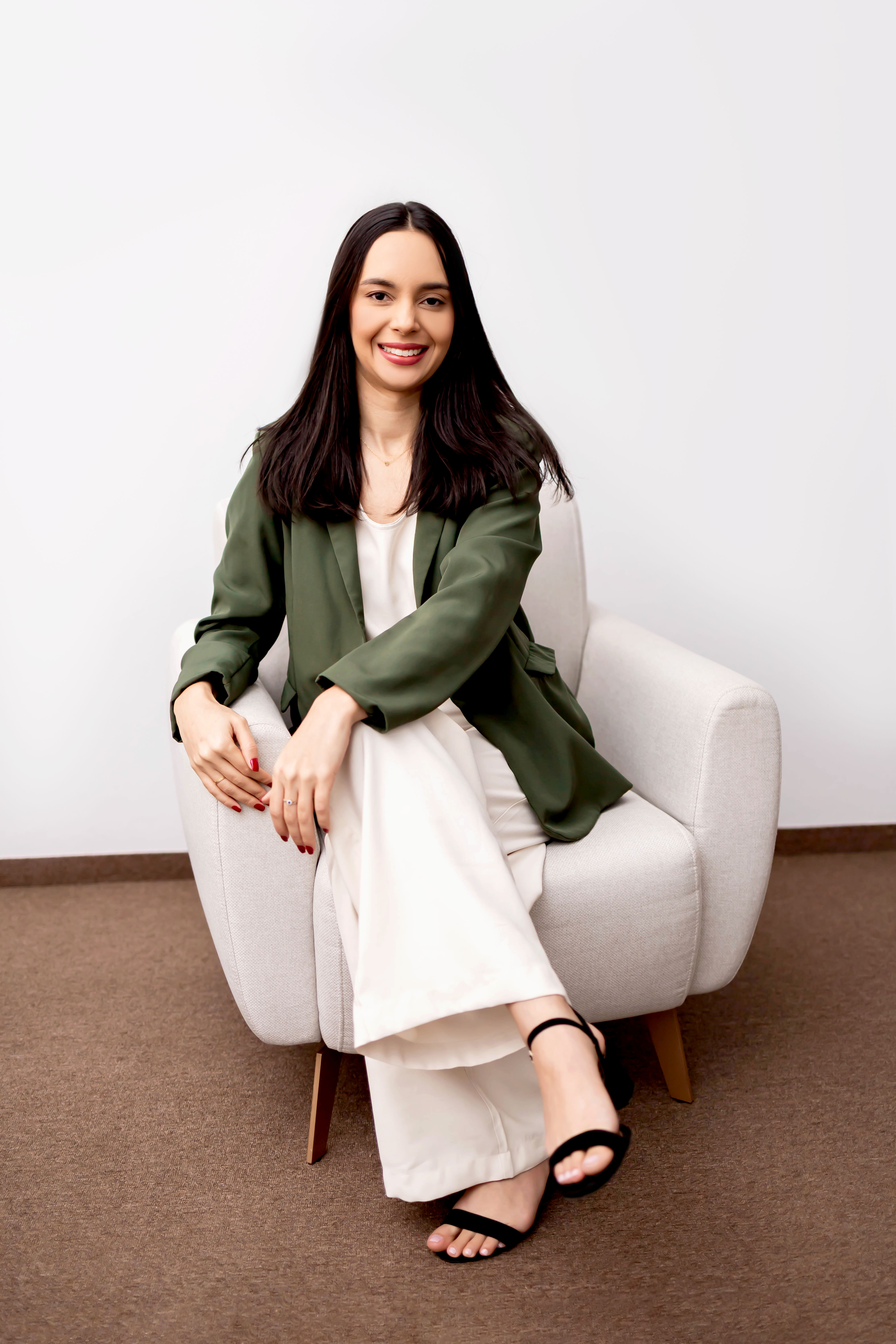Psicóloga Geovanna Araújo sentada em poltrona com blazer verde